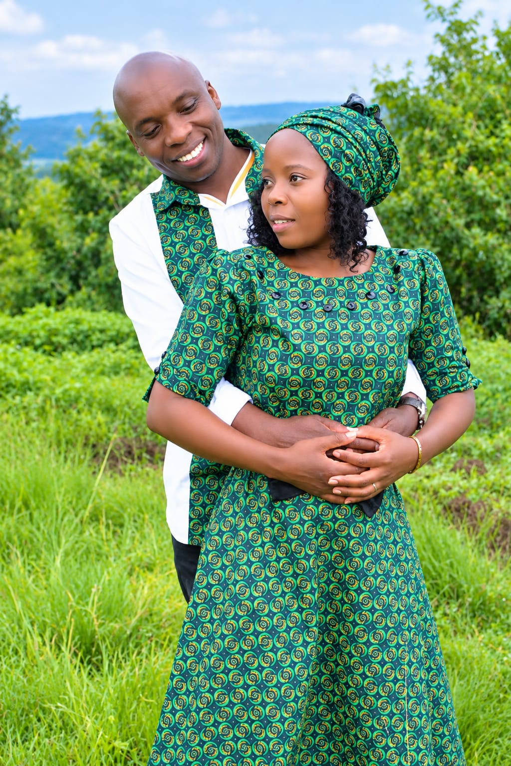 Mazwi and Thabsile embracing on a green hillside, both dressed in matching green shweshwe outfits.